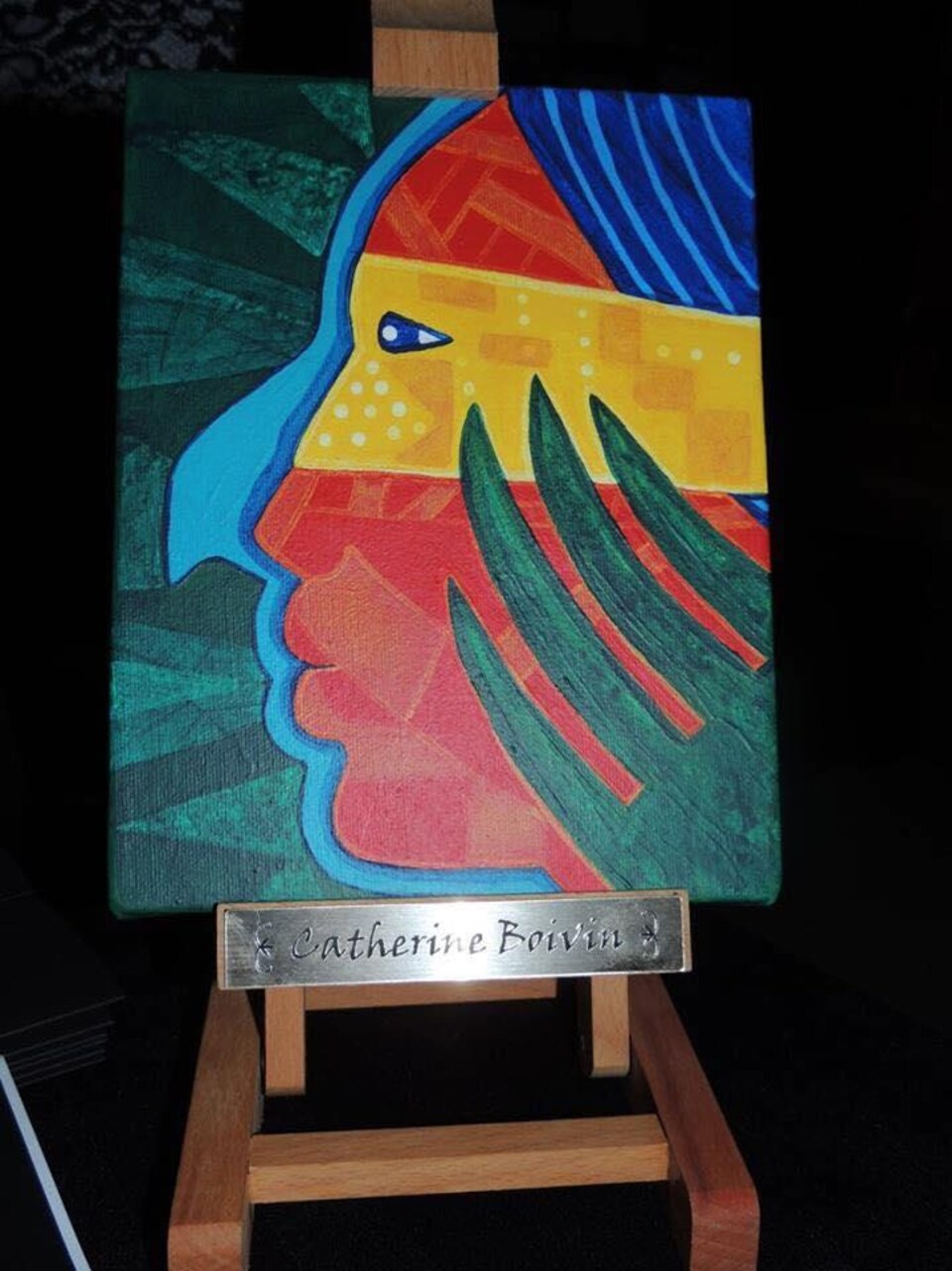Un tableau rempli de symboles autochtones est posé sur un chevalet où il est inscrit le nom de la lauréate du prix Manitou-Kiuna 2018, Catherine Boivin.
