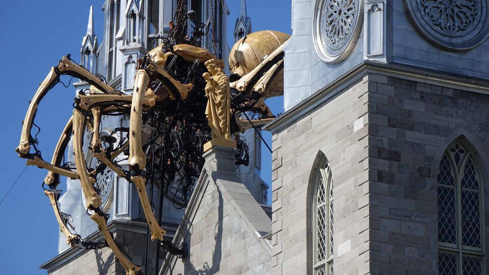 Une araignée géante mécanique perchée sur une église à l'aide d'une grue