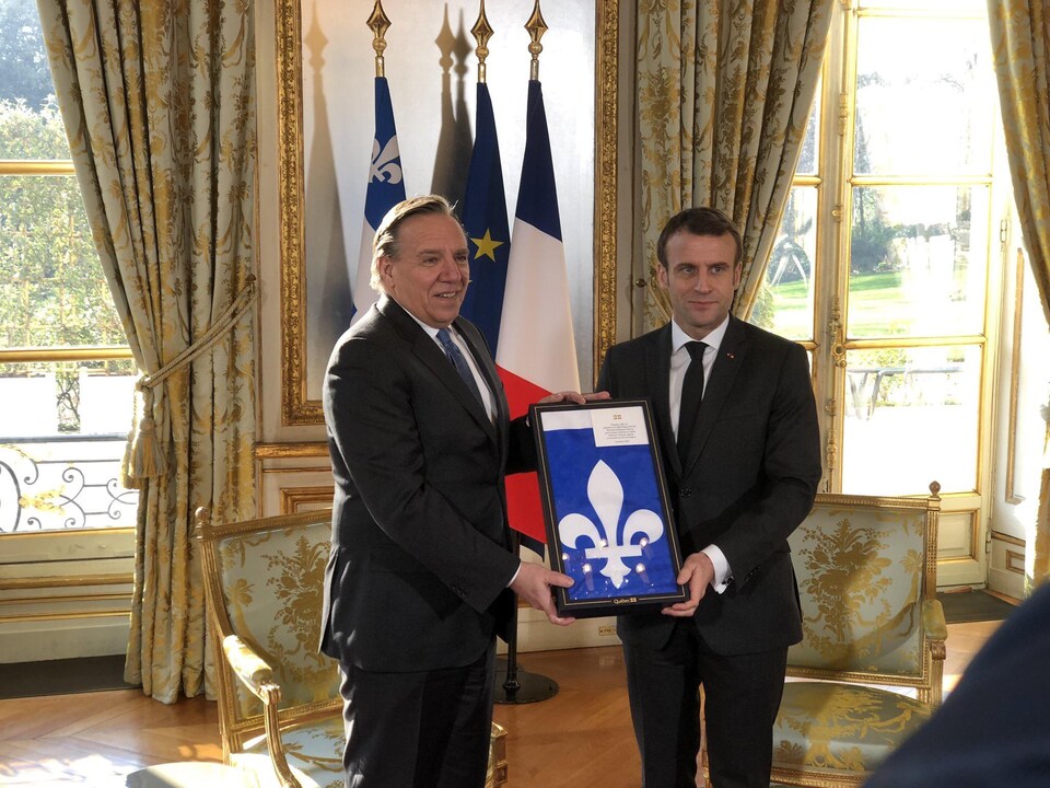 François Legault et Emmanuel Macron tiennent un drapeau du Québec encadré en souriant à la caméra.