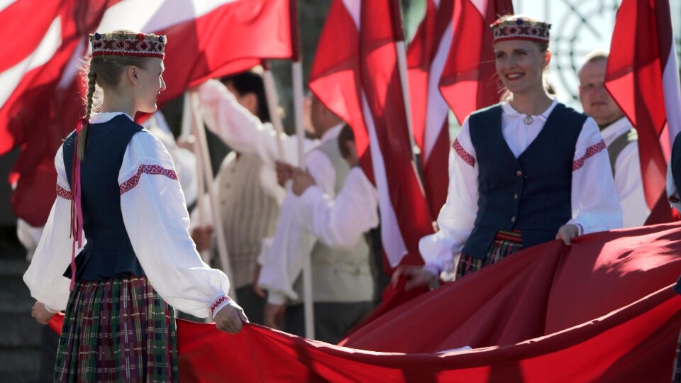 Des femmes habillées en costumes traditionnels de la Lettonie marchent avec des drapeaux. 