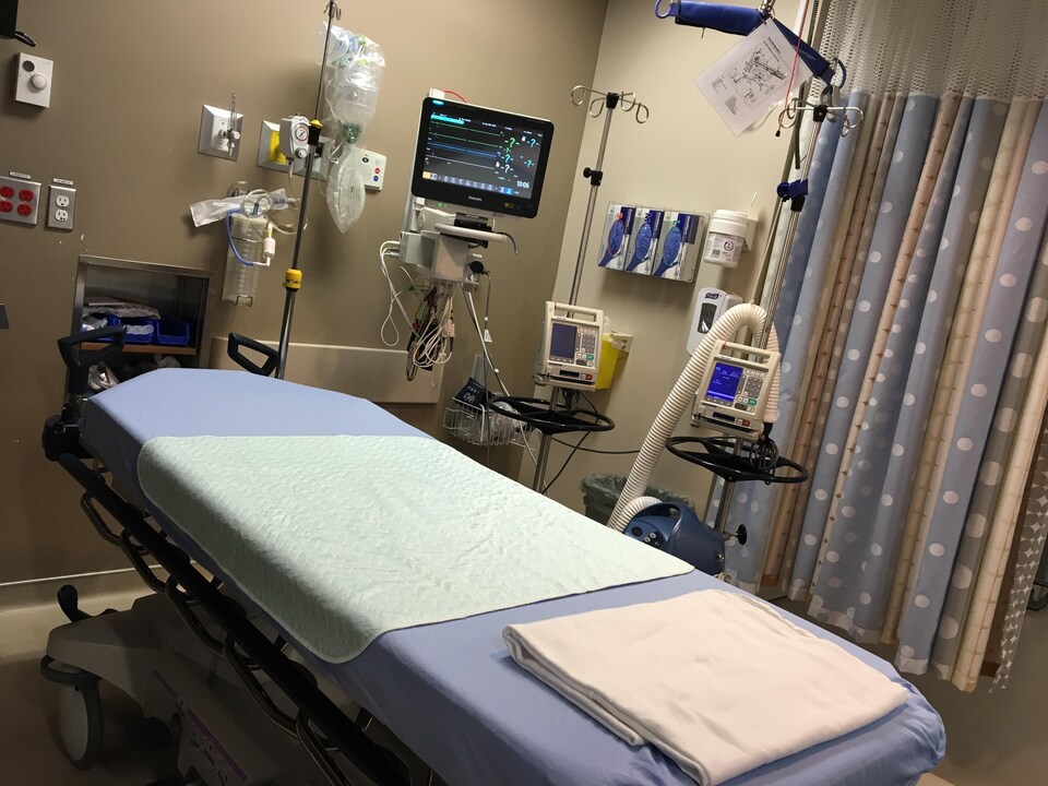 Un lit d'hôpital vide avec des machines et de l'équipement de soins médicaux ainsi qu'un moniteur. 