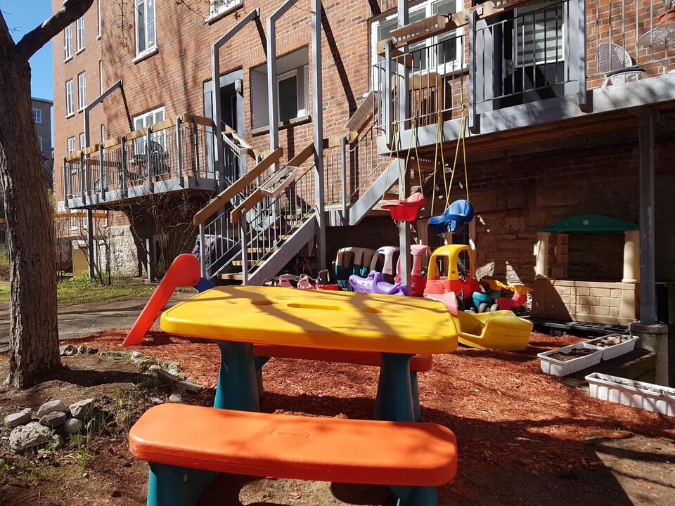 Cour arrière d’une coopérative d’habitation du centre-ville de Québec. On aperçoit une table et des jeux en plastique pour enfants.