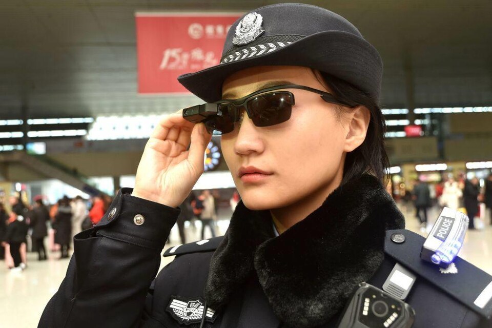 Une policière touche ses lunettes fumées de haute technologie dans une gare de train. 