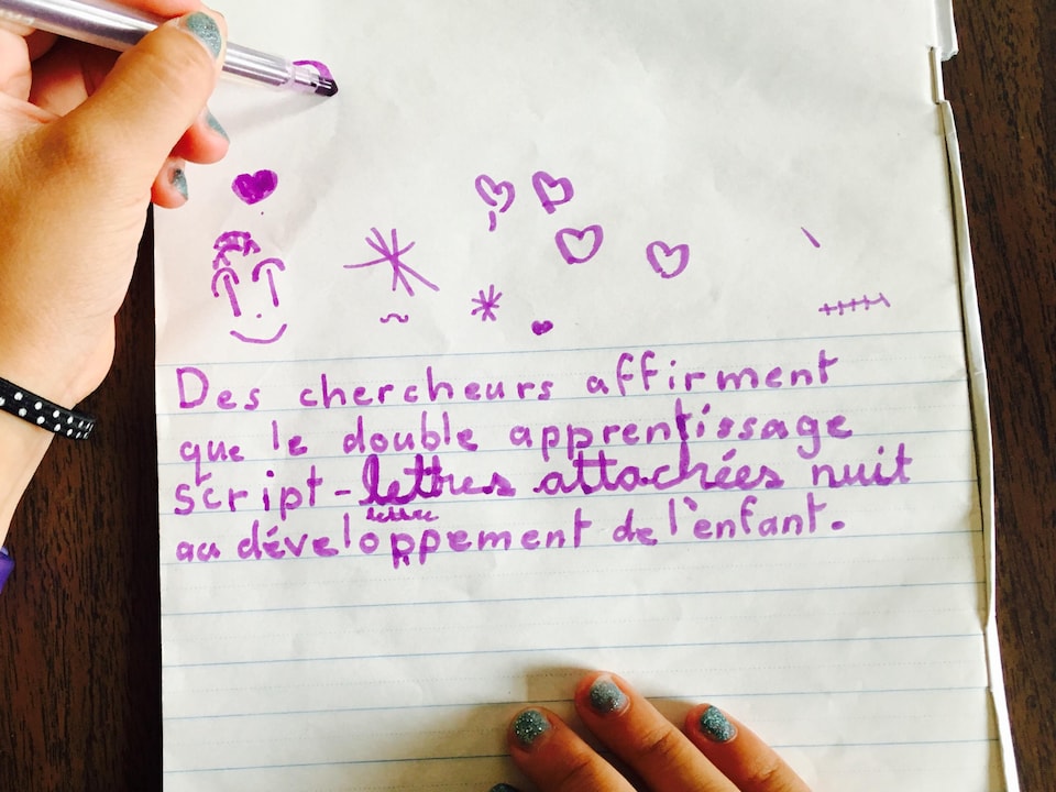 Une écolière écrit à la main en lettres détachées et attachées dans un cahier.