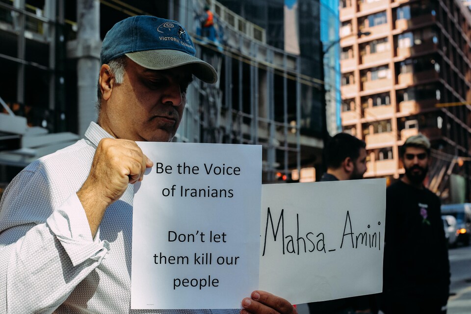 Un manifestant à Vancouver tient une pancarte au nom de Mahsa Amini et une autre où on peut lire «soyez la voix des Iraniens, ne les laissez pas tuer notre peuple». 