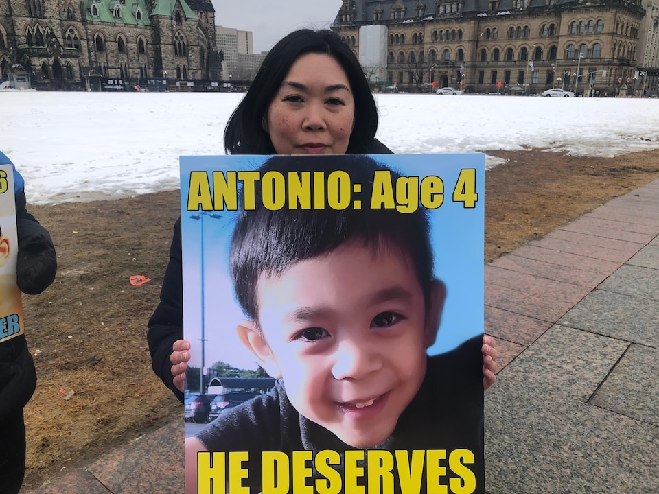 Une femme tient une pancarte avec la photo d'un jeune garçon de quatre ans. 