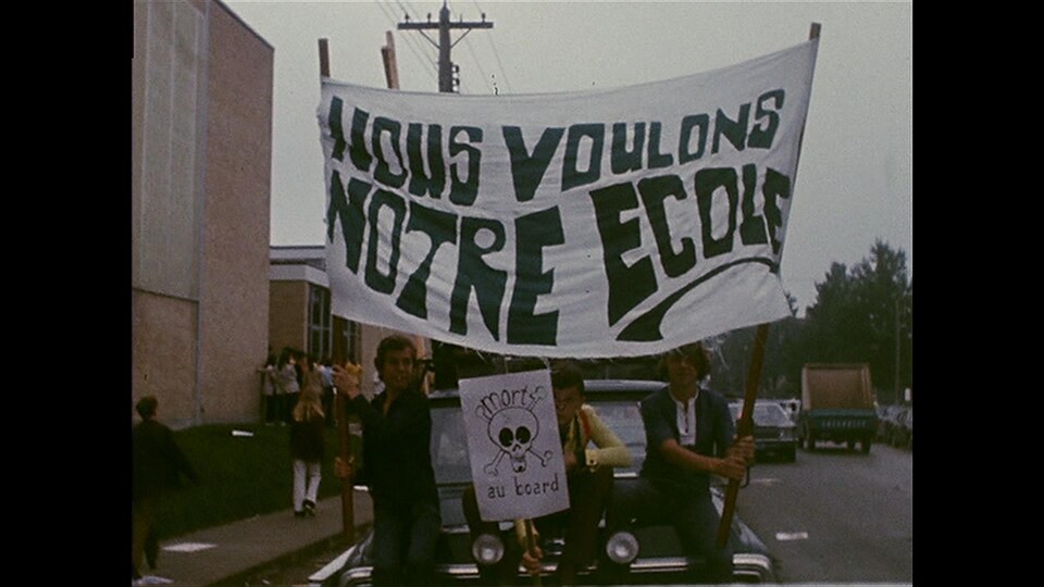 Des adolescents tiennent à la main grande bannière sur laquelle on peut lire « Nous voulons notre école ». 