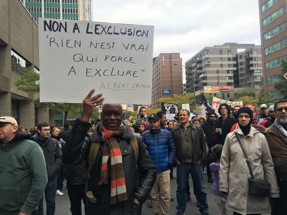 Des manifestants dont l'un tient une pancarte sur laquelle on peut lire « Non à l'exclusion. Rien n'est vrai qui force à exclure. Albert Camus ».