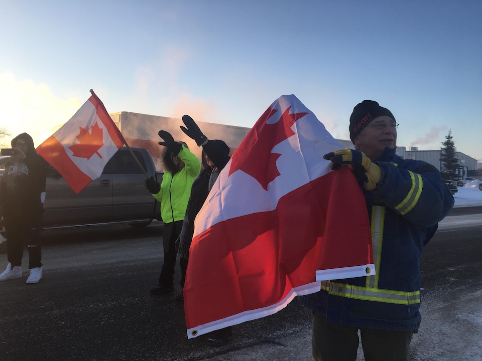 Des manifestants saluent les camions sur le départ avec des drapeaux canadiens dans les mains.