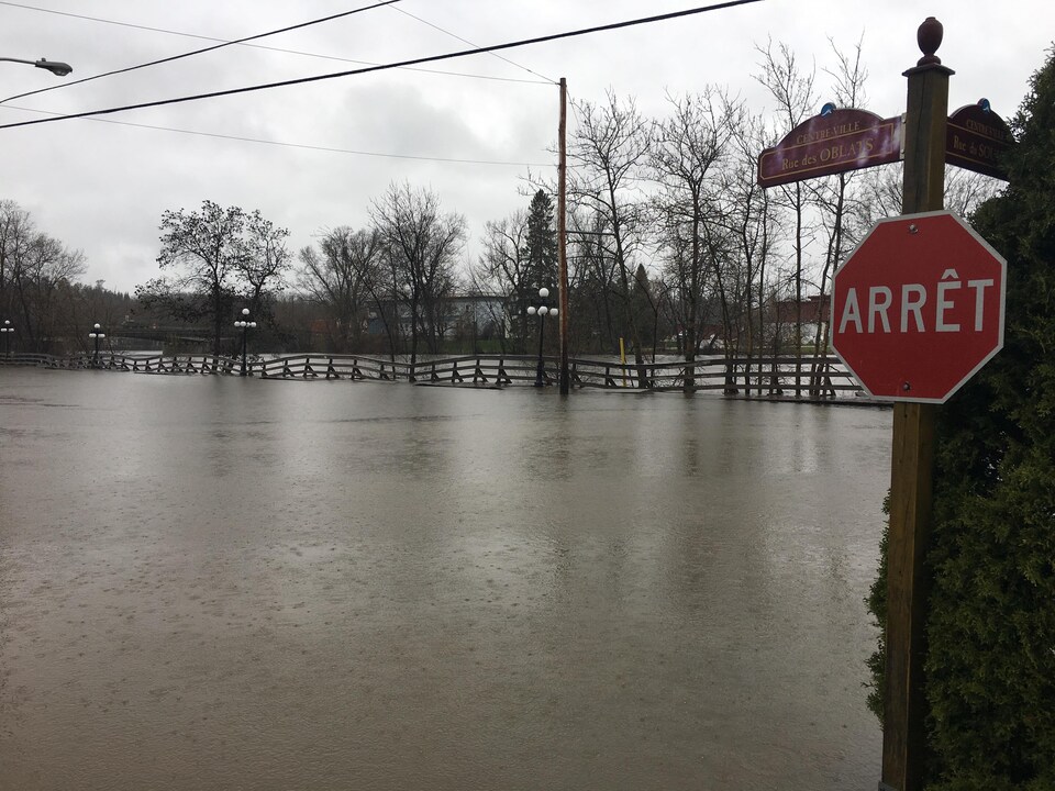 Un signe ''Arrêt'' avec une rue inondée à l'arrière.