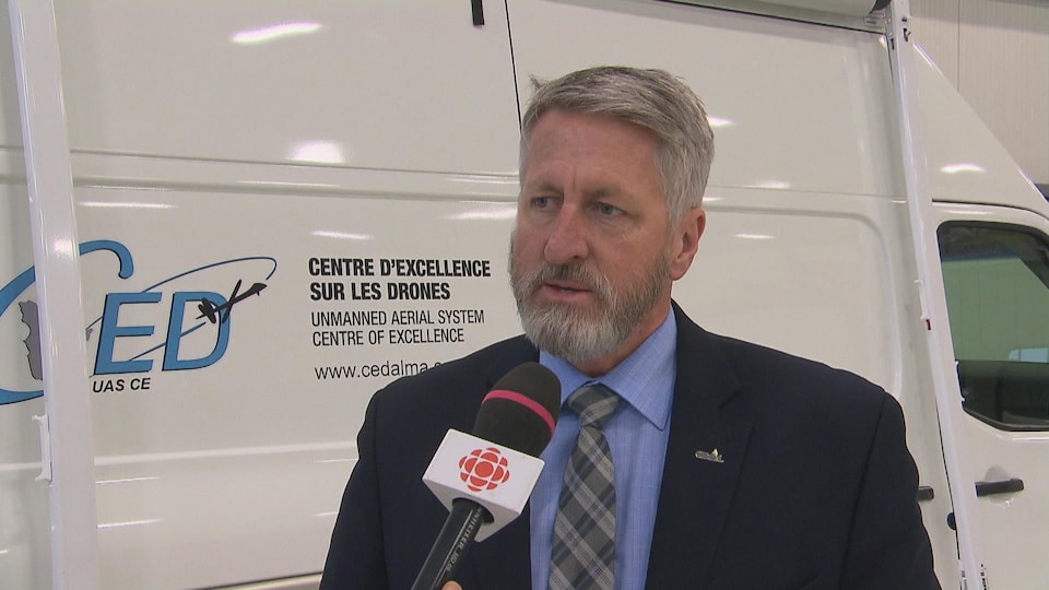 Un homme en entrevue à Radio-Canada. Il est devant un véhicule à l'effigie du Centre national des drones.