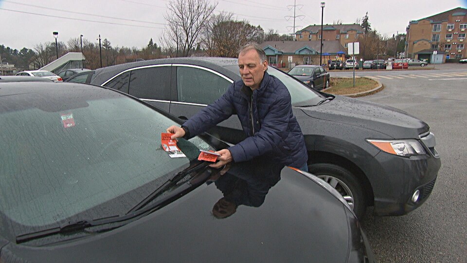 Un homme dépose un tract sur le pare-brise d'une voiture.