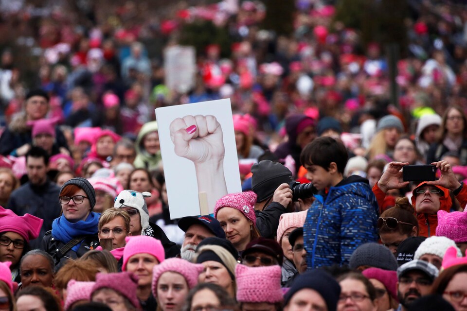 Une manifestante brandit une pancarte montrant un poing féminin levé et plusieurs autres portent un « Pussyhat », un chapeau en laine rose avec des oreilles de chat, en référence à des propos de Donald Trump diffusés pendant la campagne présidentielle.