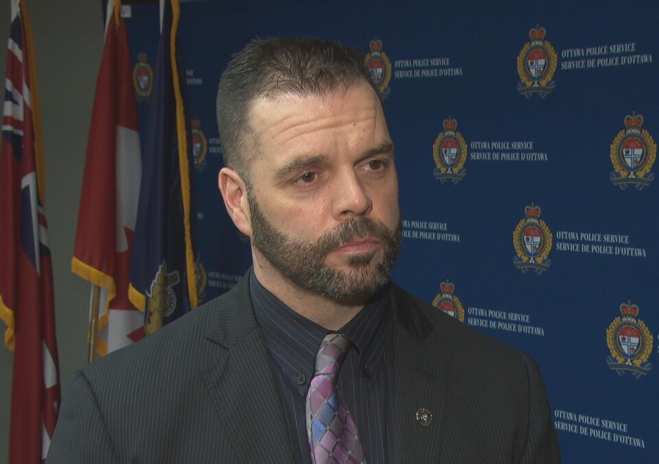 Mark Patterson donne une entrevue à Radio-Canada dans les locaux du Service de police d'Ottawa, alors qu'en arrière-plan se trouvent plusieurs logos du SPO.