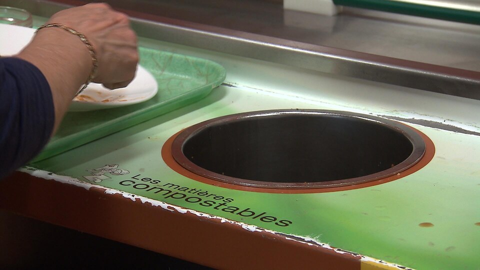 Une personne montre du doigt une poubelle pour matières compostables.