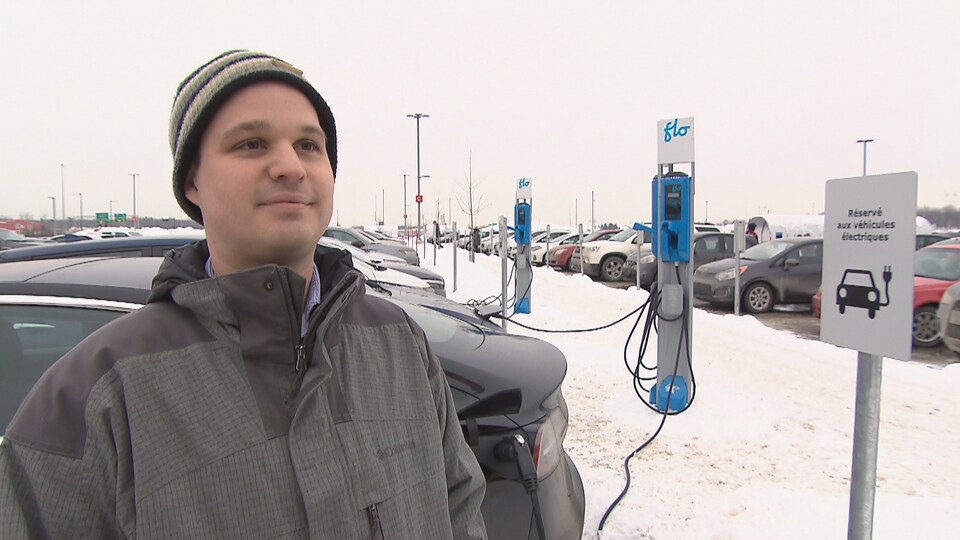 Maxime Roussel, délégué régional pour l'Association des véhicules électriques du Québec, est à l'avant-plan devant des bornes de recharge pour véhicules électriques.
