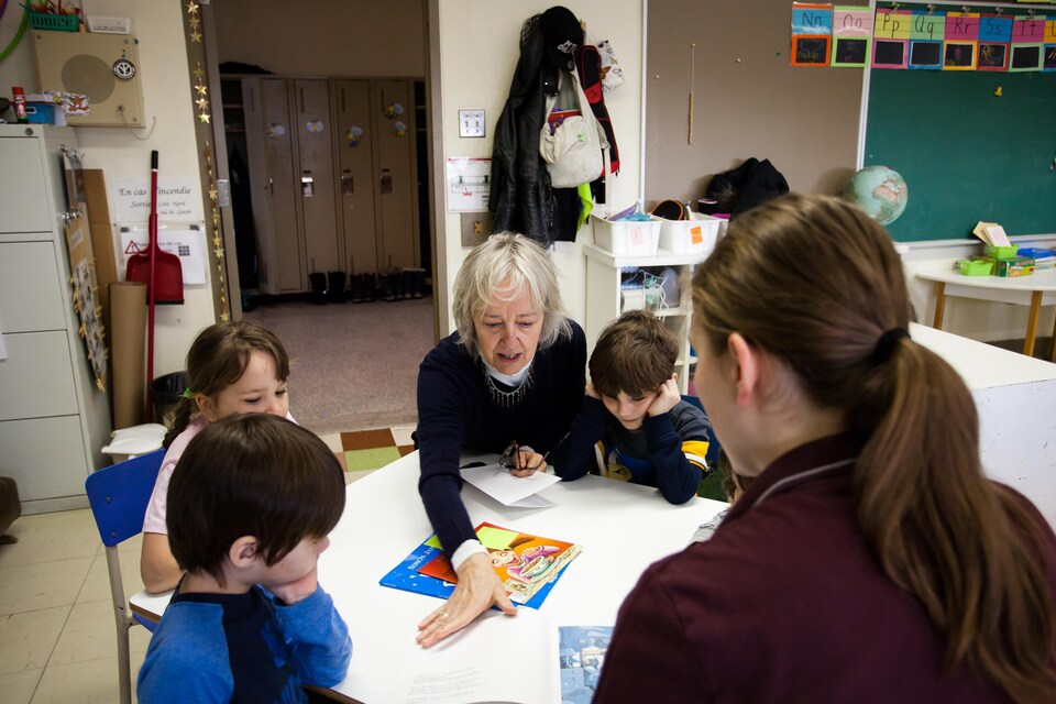 De jeunes élèves de la maternelle sont attablés autour d'une table basse couverte de contes, alors que l'aînée Suzanne Lavallée tourne la page d'un livre.
