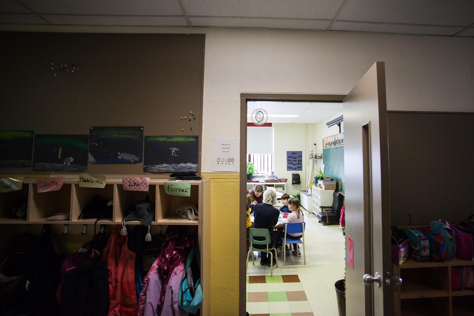 À travers la porte d'une classe, on aperçoit de jeunes élèves de la maternelle qui écoutent Suzanne Lavallée et Lydia De Melo.