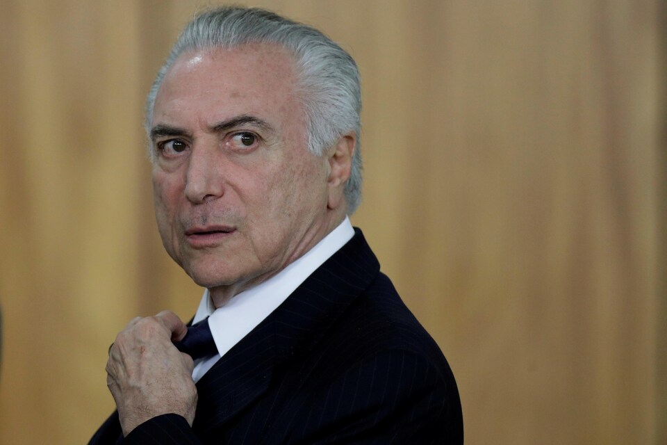 Michel Temer, qui porte un veston noir et qui tient sa cravate de la main gauche, regarde au loin.