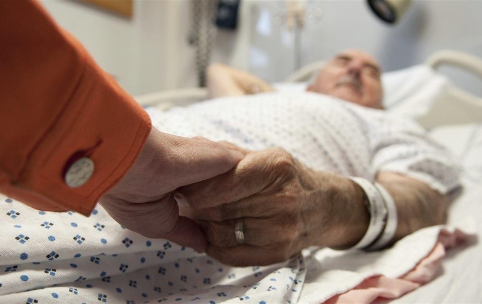 On voit un vieil homme vulnérable sur une civière d'hôpital à qui on tient la main.