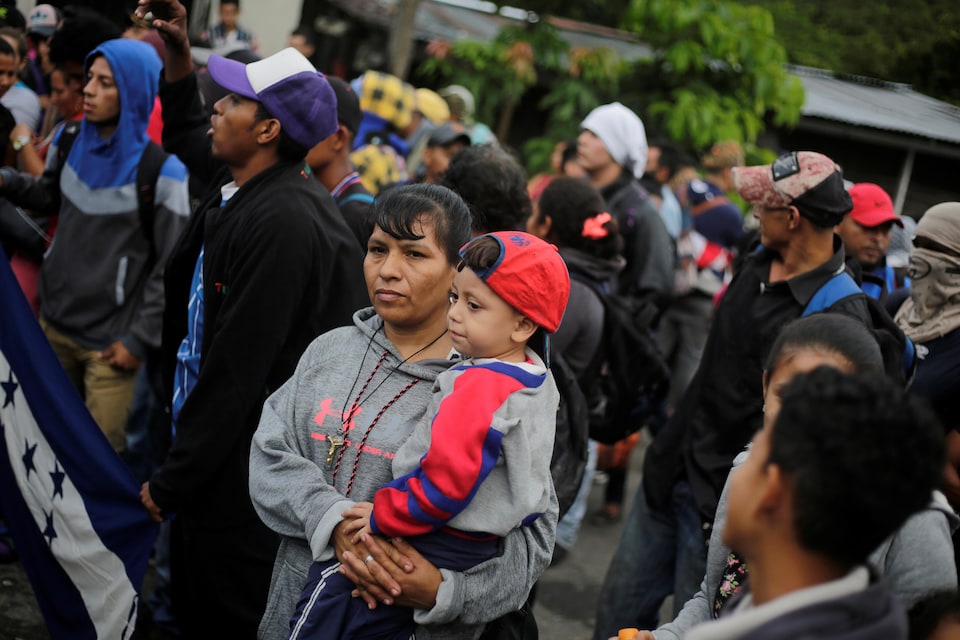 Des dizaines de migrants, dont une femme tenant un enfant dans ses bras, attendent à la frontière.