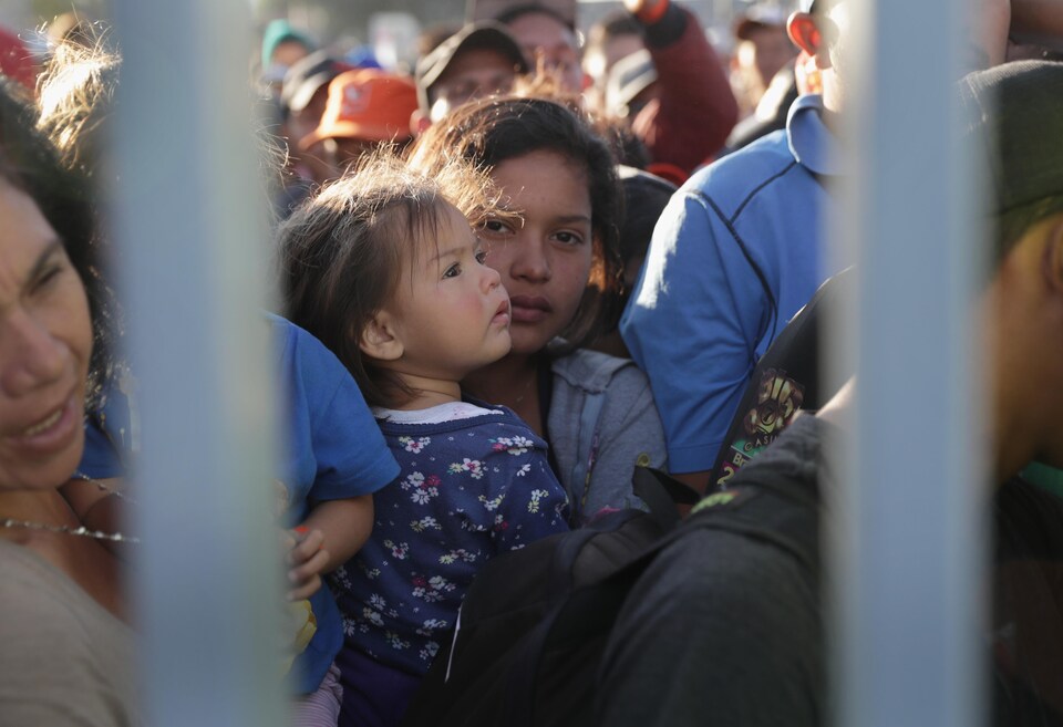 Des gens sont entassés derrière des barreaux, au centre de la photo, une jeune femme tient une enfant dans ses bras.