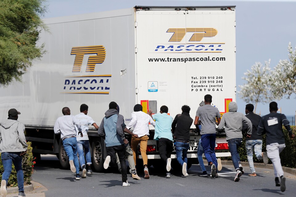 Une dizaine de migrants courent derrière un camion de marchandise. 