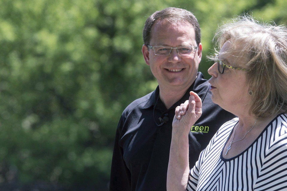 Mike Schreiner, portant un t-shirt noir, regarde Elizabeth May, vêtue d'une robe.