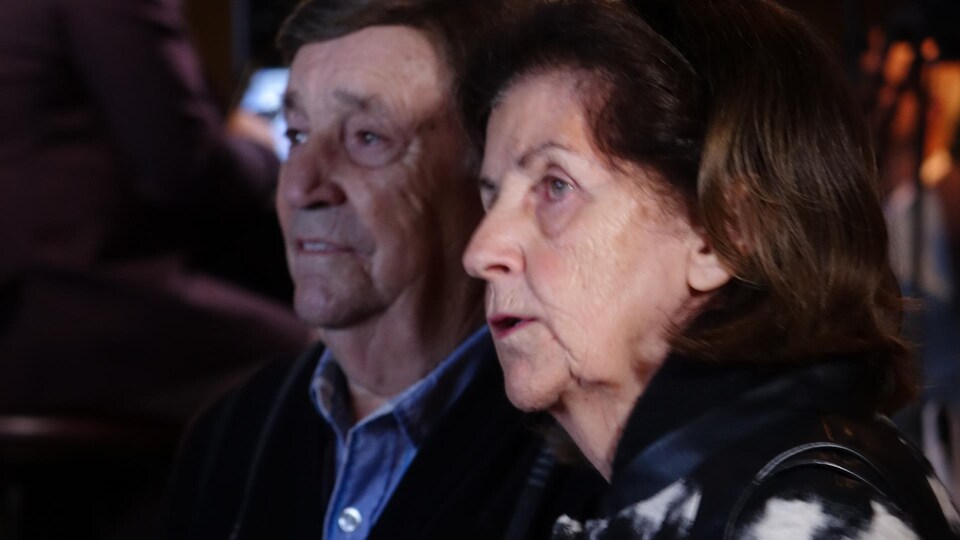 Un homme et une femmes âgés regardent la défaite de leur parti sur deux écrans géants.