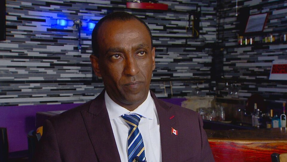 Moe Tesfay devant un bar orné de bouteilles d'alcool. 