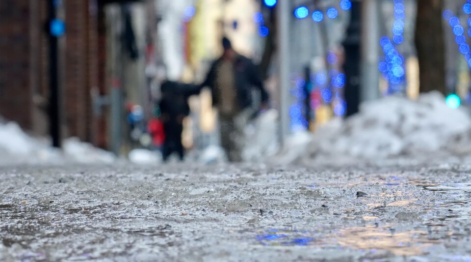 La glace recouvre un trottoir où deux passants tentent de circuler.