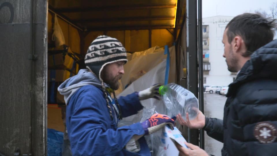 Un homme portant une tuque ramasse les matières recyclables que lui tend un autre homme pour les mettre dans son camion.