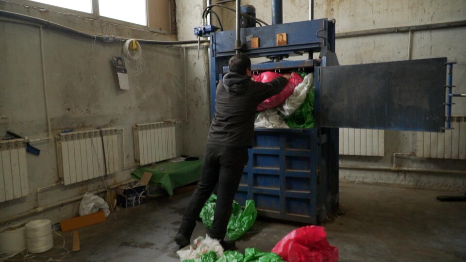 Un homme rempli un compacteur industriel de déchets en plastique dans une usine.