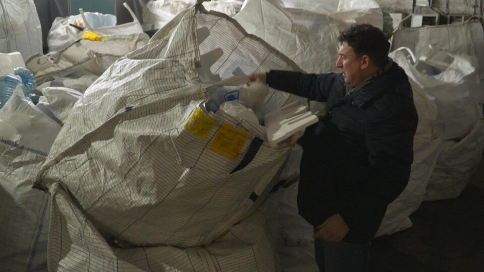 Un homme fouille dans un grand sac rempli de matières recyclables.