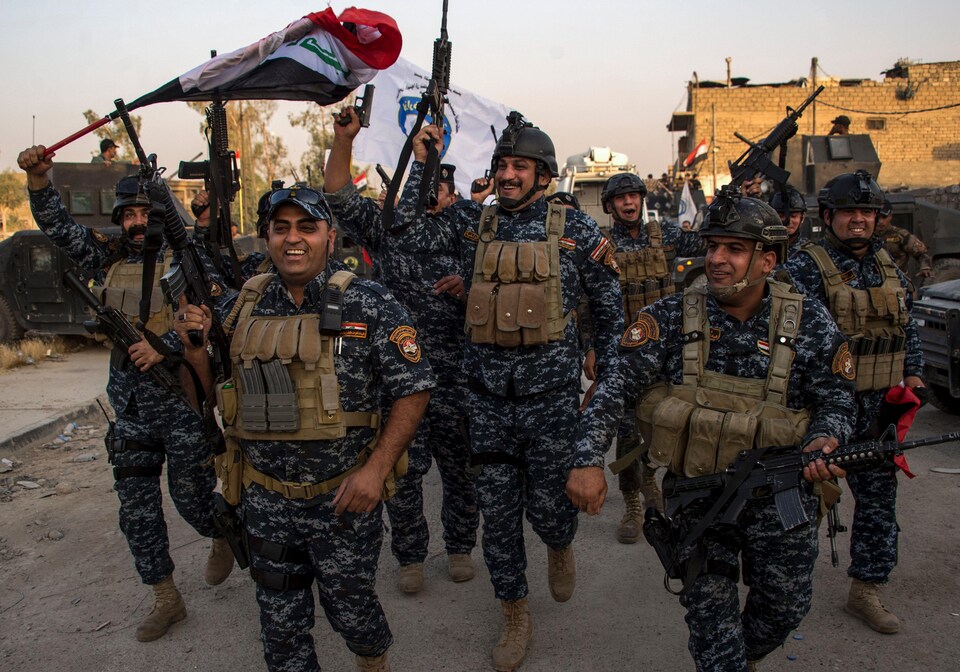 Des agents de la police fédérale irakienne manifestent leur joie en brandissant leurs armes et des drapeaux.