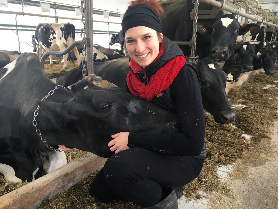 Une agricultrice sourit à la caméra, tout en caressant une vache.