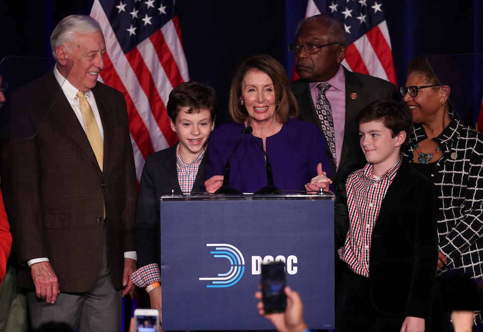 Nancy Pelosi, souriante, derrière un podium, entourée de quelques personnes, dont deux enfants.