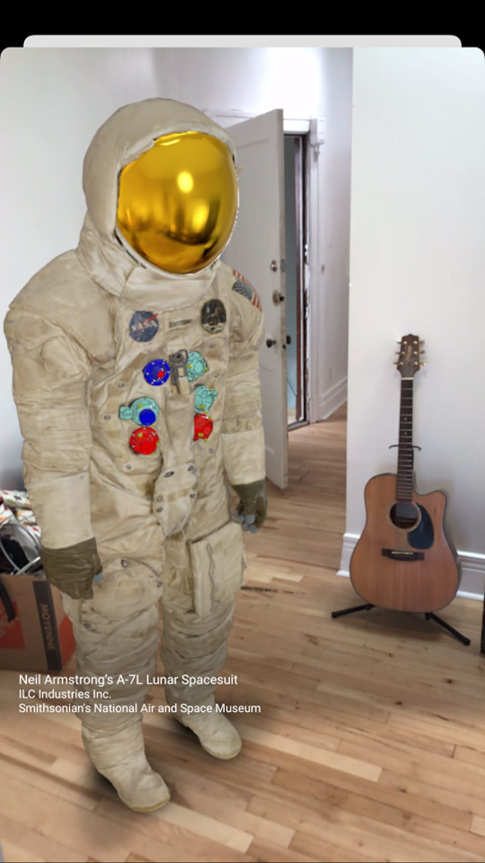 Une combinaison spatiale dans une pièce, à côté d'une guitare. 