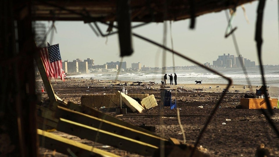 Des infrastructures brisées et un drapeau américain déchiré se trouvent le long d'une plage jonchées de déchets.