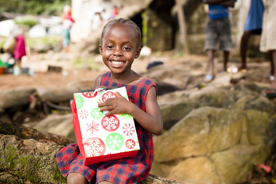 Une fillette africaine sourit et tient un sac-cadeau.