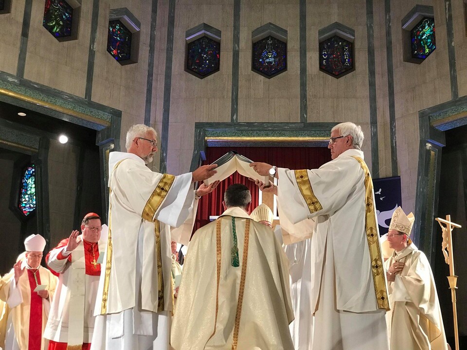 Deux évêques tiennent un livre au-dessus de la tête d'un évêque qui se tient à genoux.
