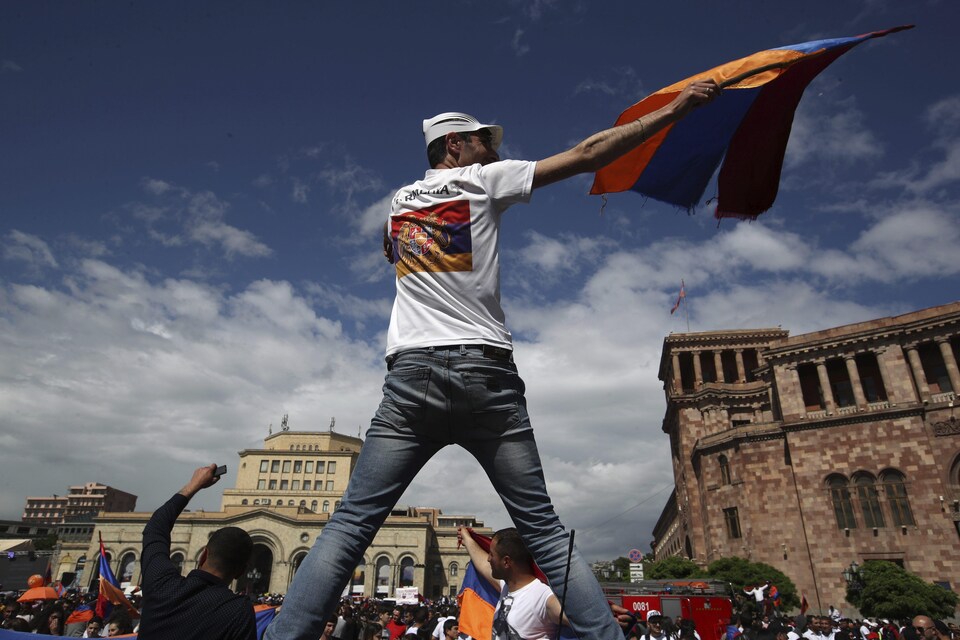 Un homme vu de dos brandit le drapeau arménien, aussi visible sur son t-shirt.