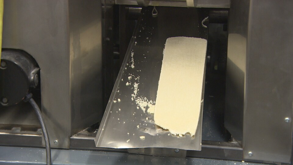 Un morceau de pâte sort d'une machine industrielle qui pétrie la pâte. 