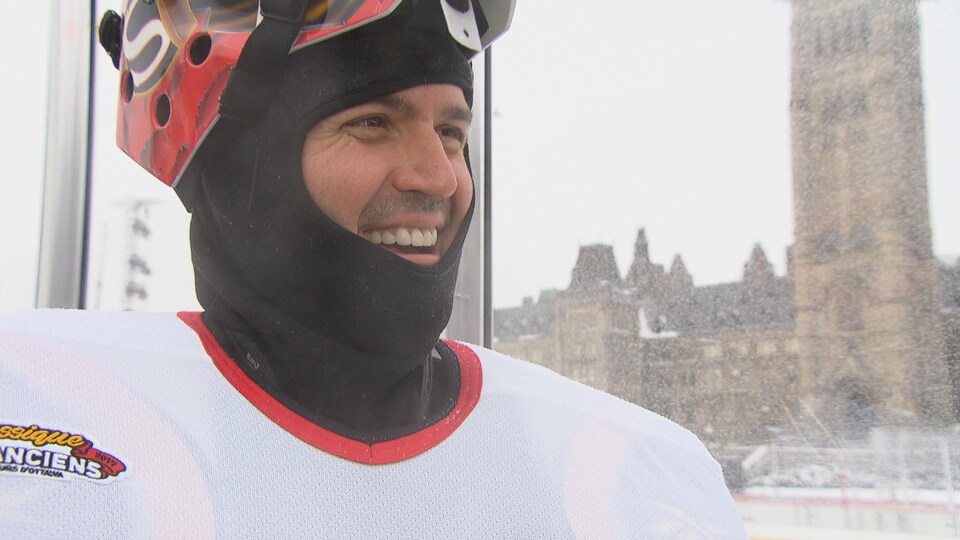 Un homme portant de l'équipement de hockey sourit devant le parlement
