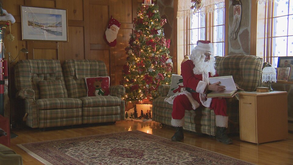 André Saindon vêtu en père Noël ouvre un livre dans sa maison.
