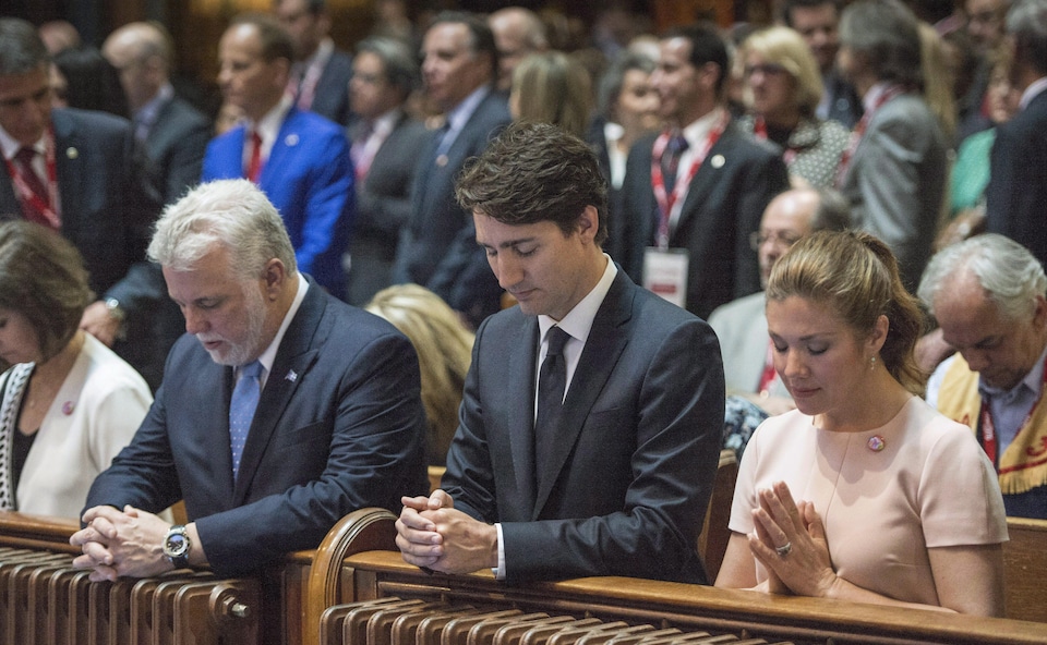 Les premiers ministres Philippe Couillard et Justin Trudeau, ainsi que Sophie Grégoire, prient lors d'une messe.