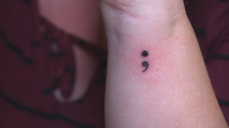 Un point virgule est tatoué sur un poignet.