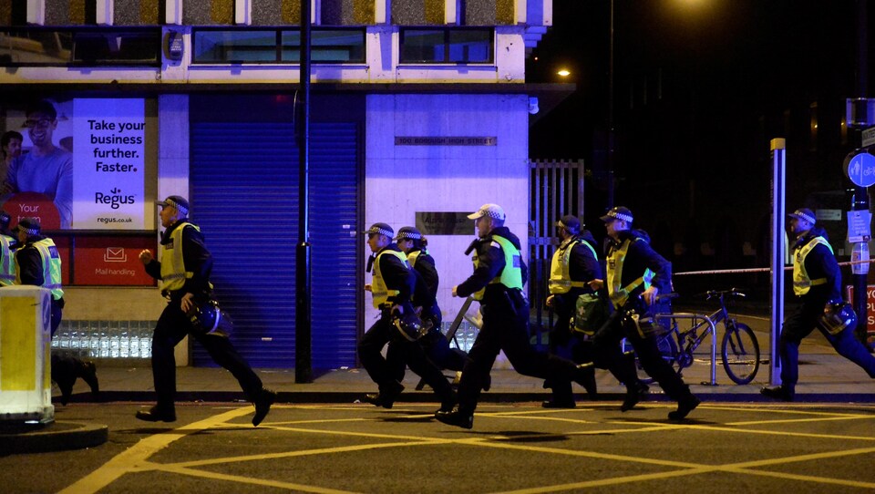 Des policiers portant un dossard jaune courent dans une rue, la nuit.