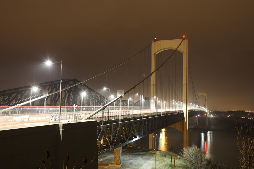 Le pont Pierre-Laporte, vu de la rive nord du fleuve Saint-Laurent, la nuit. Les phares du trafic automobile forment des traits lumineux grâce à l'exposition longue.