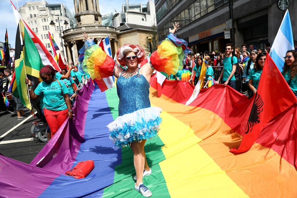 Une drag queen défile sur un drapeau arc-en-ciel.